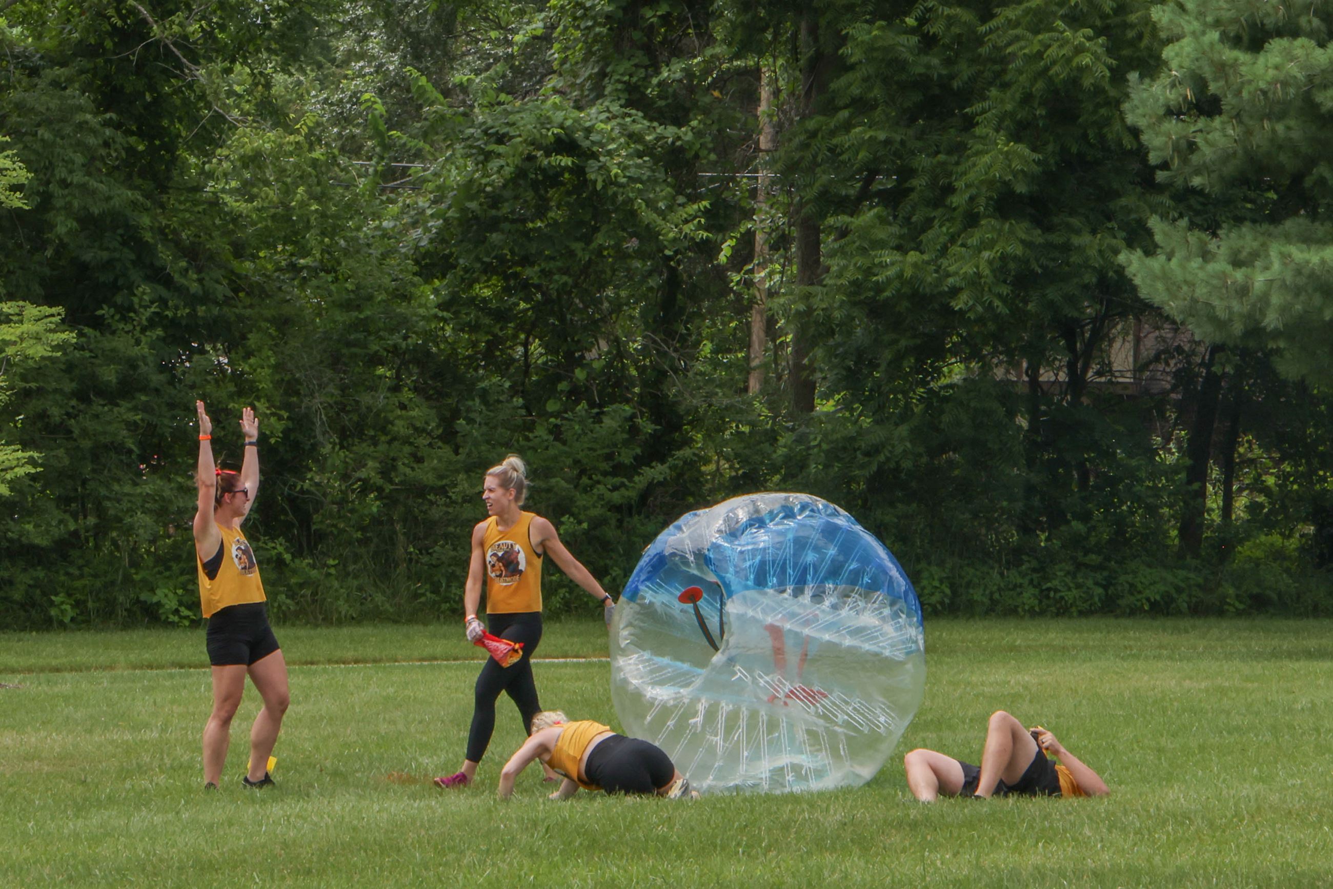 Four people in yellow shirts cheer after completing an obstacle course in a blow-up bubble